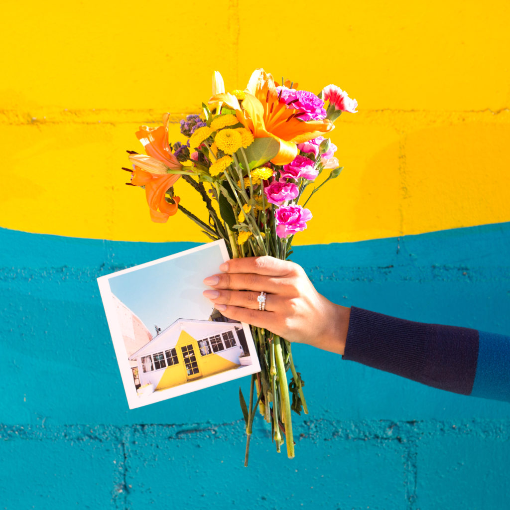 Women holding flowers and a photograph in front of a colorful wall
