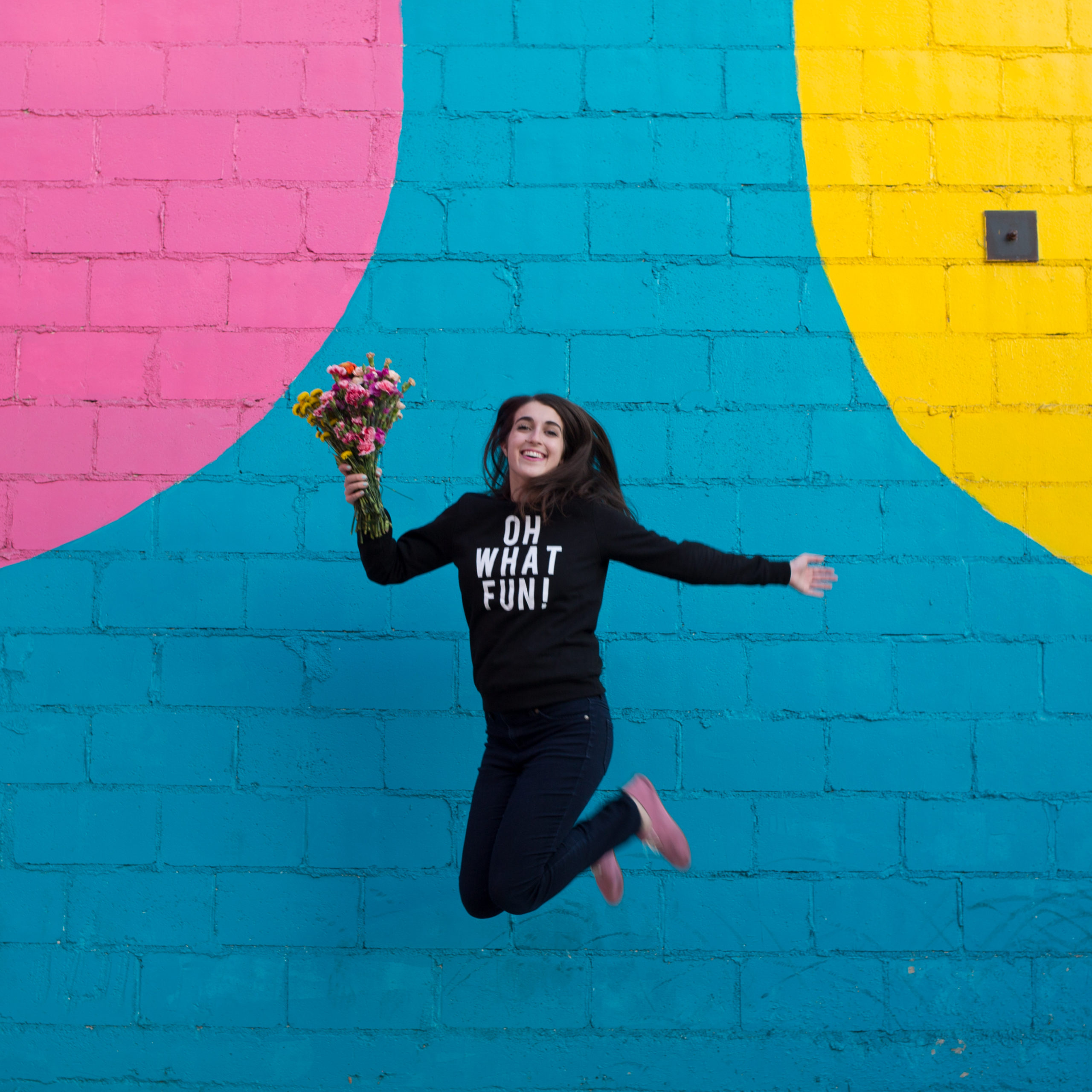 woman jumping with flowers in front of blue wall