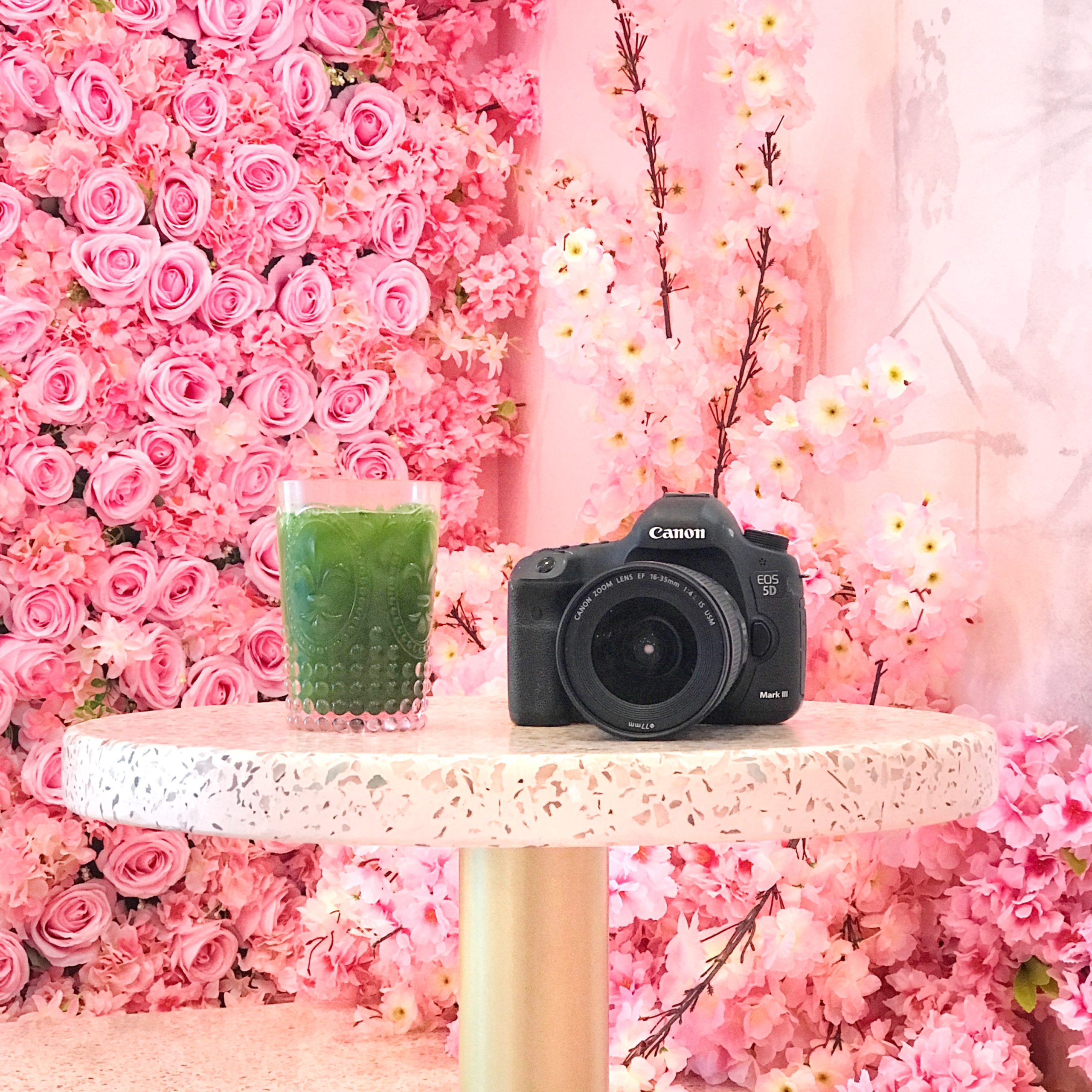 photo of a matcha and canon camera sitting on a terrazzo table in front of a pink flower wall