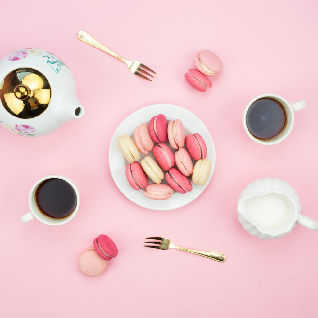 overhead shot of coffee, macarons, gold forks, teapot