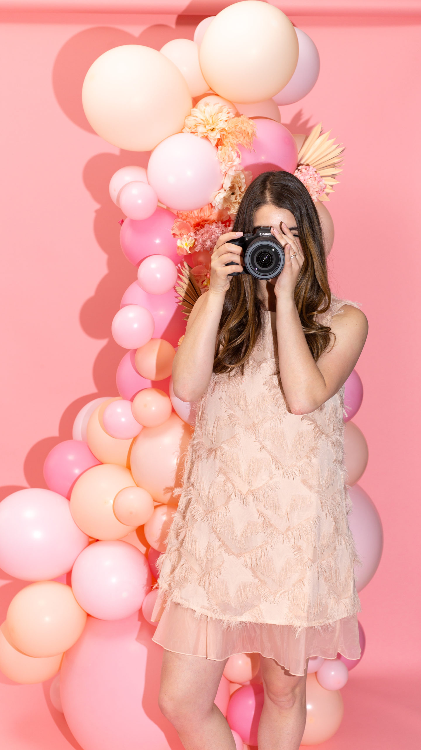photo of alisha pointing the canon eos r6 camera at the camera in front of pink balloon and floral installation