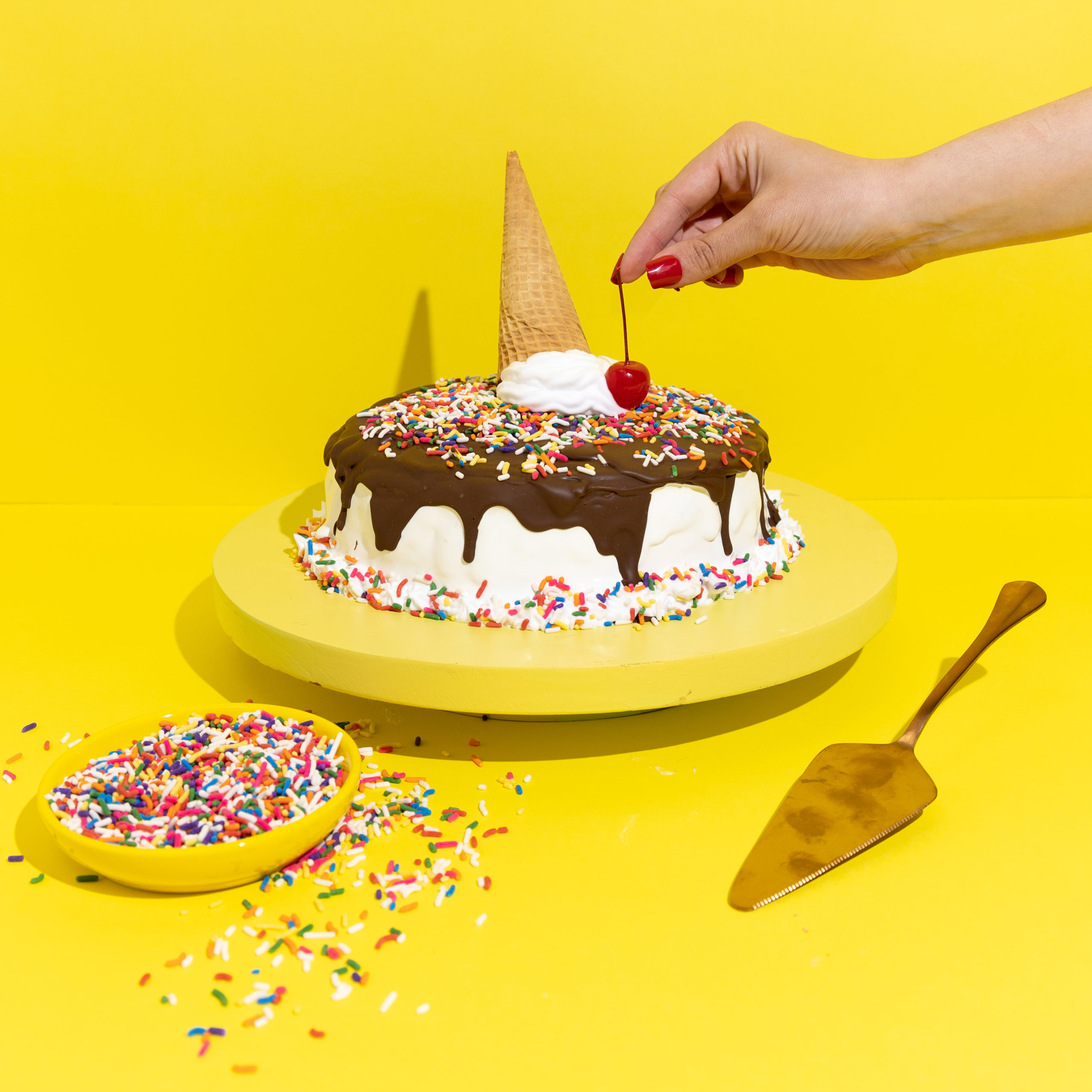 ice cream cake with sprinkles, sugar cone on top, hand placing cherry