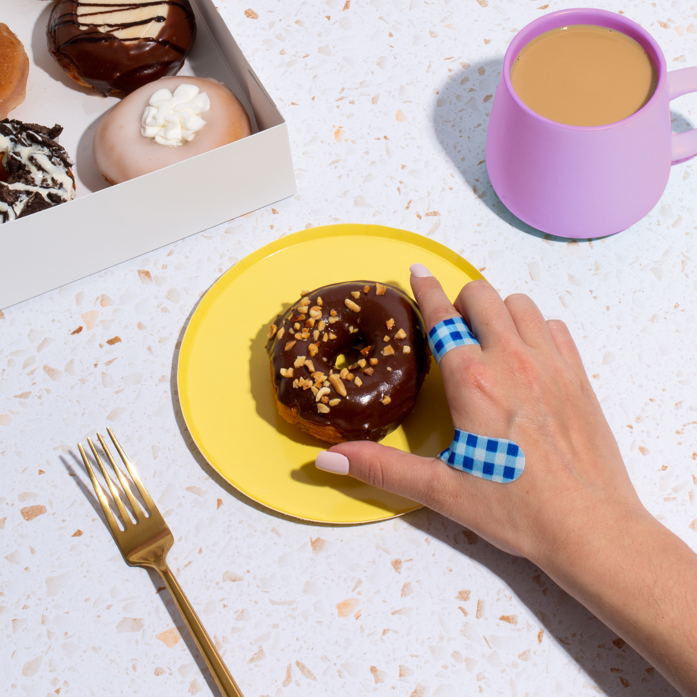 hand with blue gingham bandages on reaching in to grab donut