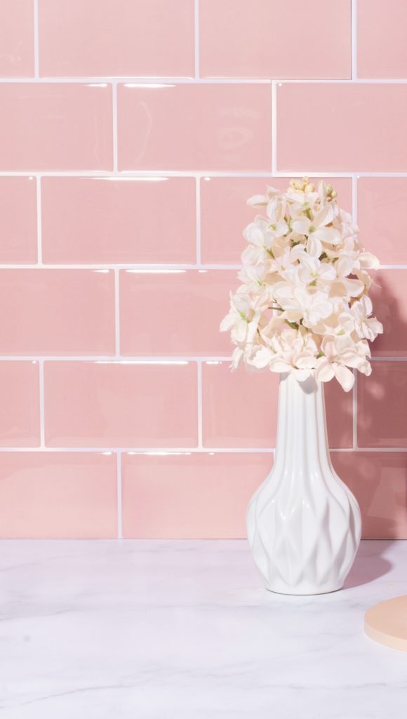 white vase with flowers in front of pink peel and stick tile backdrop