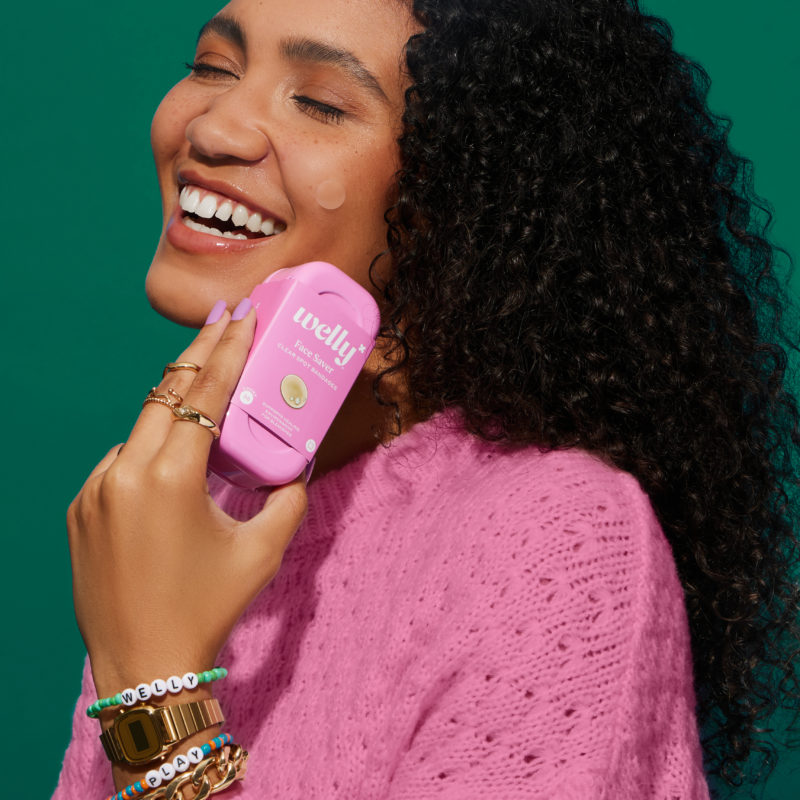 YOUNG WOMAN WITH BLACK CURLY HAIR IN PINK SWEATER HOLDING A PINK WELLY FACE SAVER BOX