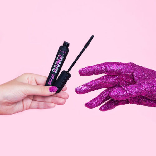 woman's hand holding mascara next to a hand covered in purple glitter