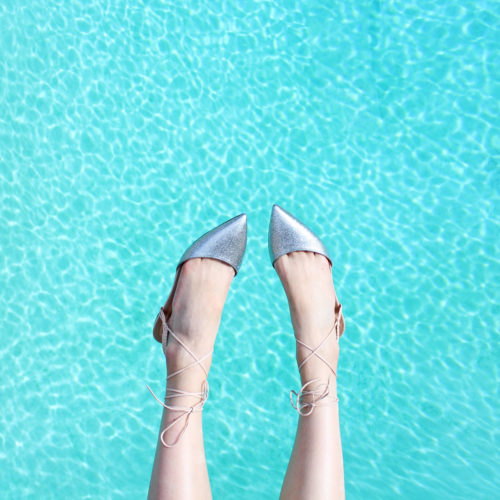woman’s feet shown wearing flats dangling over a pool