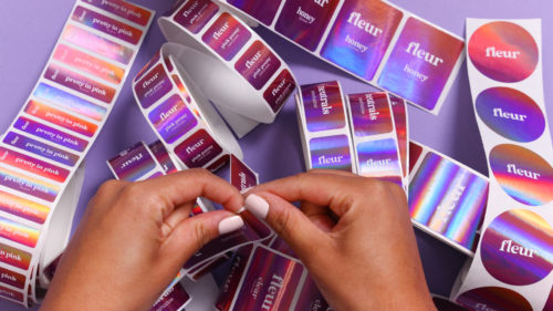 purple holographic custom avery labels laying on table with woman’s hands peeling one off 